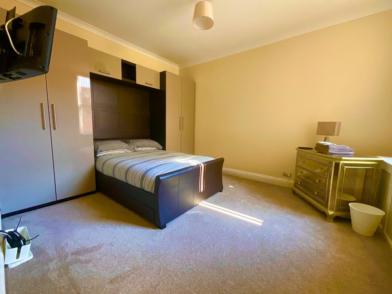 Un dormitorio con cama, armario, cómoda y una mesita de noche con lámpara.