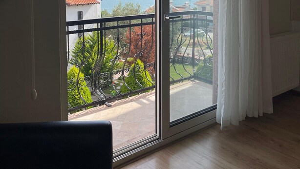 Ein Zimmer mit einer großen Schiebeglastür, die auf einen Balkon mit Blick auf das Meer und die entfernten Hügel führt.