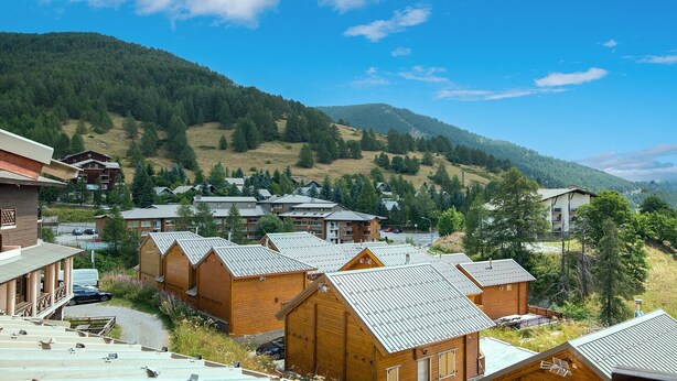 A cluster of wooden cabins with sloped roofs, set against a backdrop of a mountainous landscape. - Cute duplex studio, in the mountains, sleeps 5 (Allos)