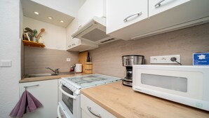 A compact kitchen with a built-in oven, microwave, and coffee maker. There is a wooden countertop, a sink, and a window above the sink. - Cute duplex studio, in the mountains, sleeps 5 (Allos)