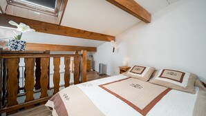A bedroom with a wooden bed frame, a quilted bedspread, and a nightstand with a lamp. - Cute duplex studio, in the mountains, sleeps 5 (Allos)
