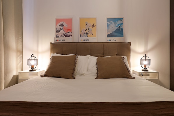 A neatly made bed with a headboard, two bedside tables with lamps, and three posters on the wall.