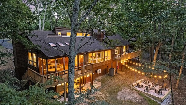 Une cabane à deux étages dotée d’une terrasse, de grandes fenêtres et d’un espace aménagé avec un foyer.