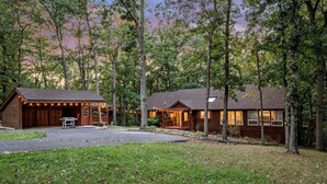 Un chalet rustique doté d’une véranda et d’un espace extérieur aménagé et abrité, le tout entouré d’arbres.
