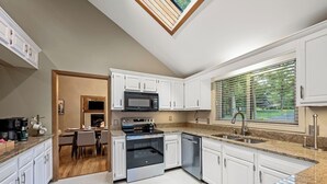 Une cuisine moderne avec des meubles blancs, un four encastré, un four à micro-ondes et une grande fenêtre avec des stores.
