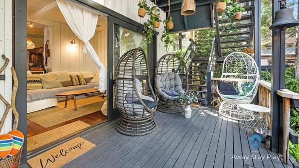 Un espace extérieur accueillant, aménagé avec des fauteuils en osier et un banc rembourré, une terrasse en bois et un paillasson.