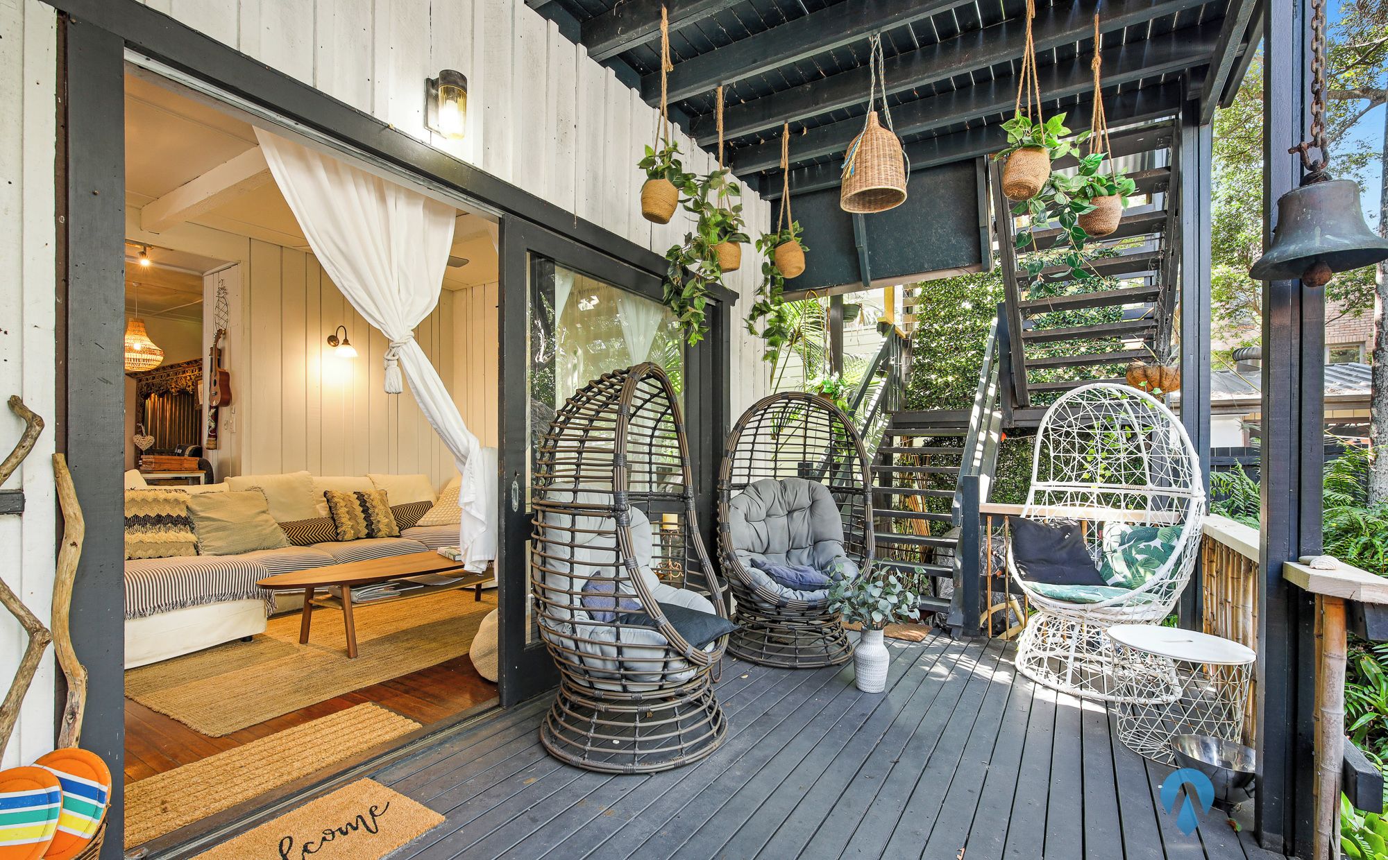 Un espace extérieur accueillant, aménagé avec des fauteuils en osier et un banc rembourré, une terrasse en bois et un paillasson.
