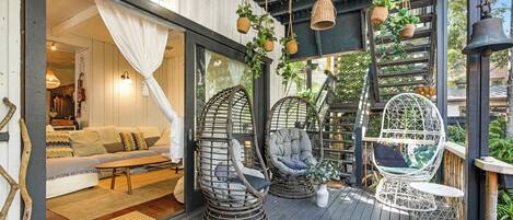 Un espace extérieur accueillant, aménagé avec des fauteuils en osier et un banc rembourré, une terrasse en bois et un paillasson.