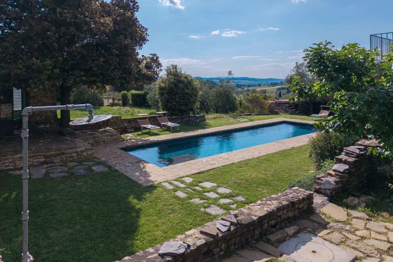 A rectangular swimming pool with a stone border, surrounded by a well-maintained lawn and stone pathway.