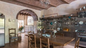Een landelijke keuken met houten meubels, een bakstenen boog en diverse keukengerei aan de muur.
