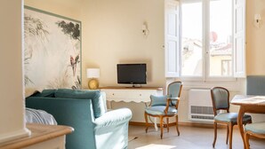 A living room with a sofa, a TV, a dining table with chairs, and a window with shutters. - Lim1939 apartment in Florence (Firenze)