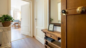 A hallway with a wooden door, a marble column, a wooden console table with a framed certificate, and a potted plant. - Lim1939 apartment in Florence (Firenze)