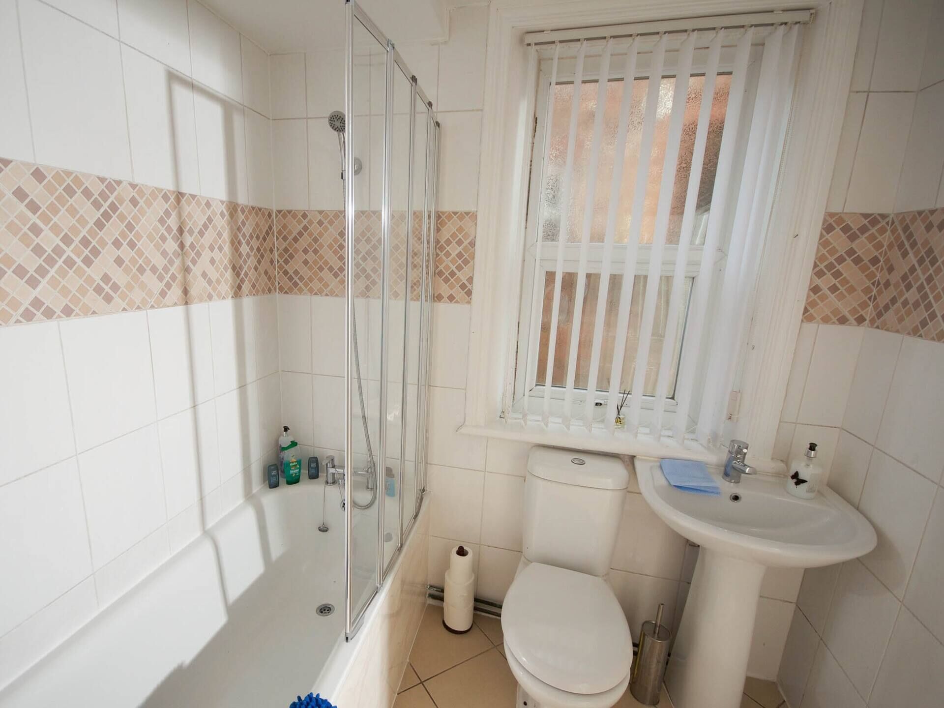 Un baño con ducha, inodoro, lavabo y ventana con persianas.