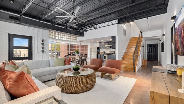 A spacious living area with a high ceiling, a staircase, and a kitchen in the background.