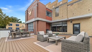 An outdoor patio area with wicker furniture, a table, and a brick building in the background.