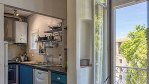 A compact kitchen with blue cabinets, a dishwasher, and a window overlooking a balcony. - Magnificent designer duplex (Avignon)