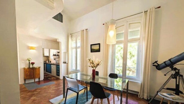 A dining area with a glass table, chairs, a vase with flowers, and a telescope on a tripod. - Magnificent designer duplex (Avignon)