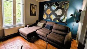 A room with a sectional sofa, a large abstract painting, and a window with a view of greenery. - Magnificent designer duplex (Avignon)