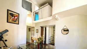 A modern dining area with a glass table and chairs, a telescope, and a staircase leading to an upper level. - Magnificent designer duplex (Avignon)