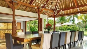 A spacious outdoor dining area with a wooden table and chairs, a thatched roof, and a view of tropical vegetation. - Kaba Kaba Estate by Elite Havens (Tabanan)