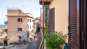 A narrow street with buildings on either side, a balcony with a metal railing, and a potted plant. - Al Belvedere A – Panoramic apartment in the Castelli Romani (Rocca di Papa) (Rocca di Papa)