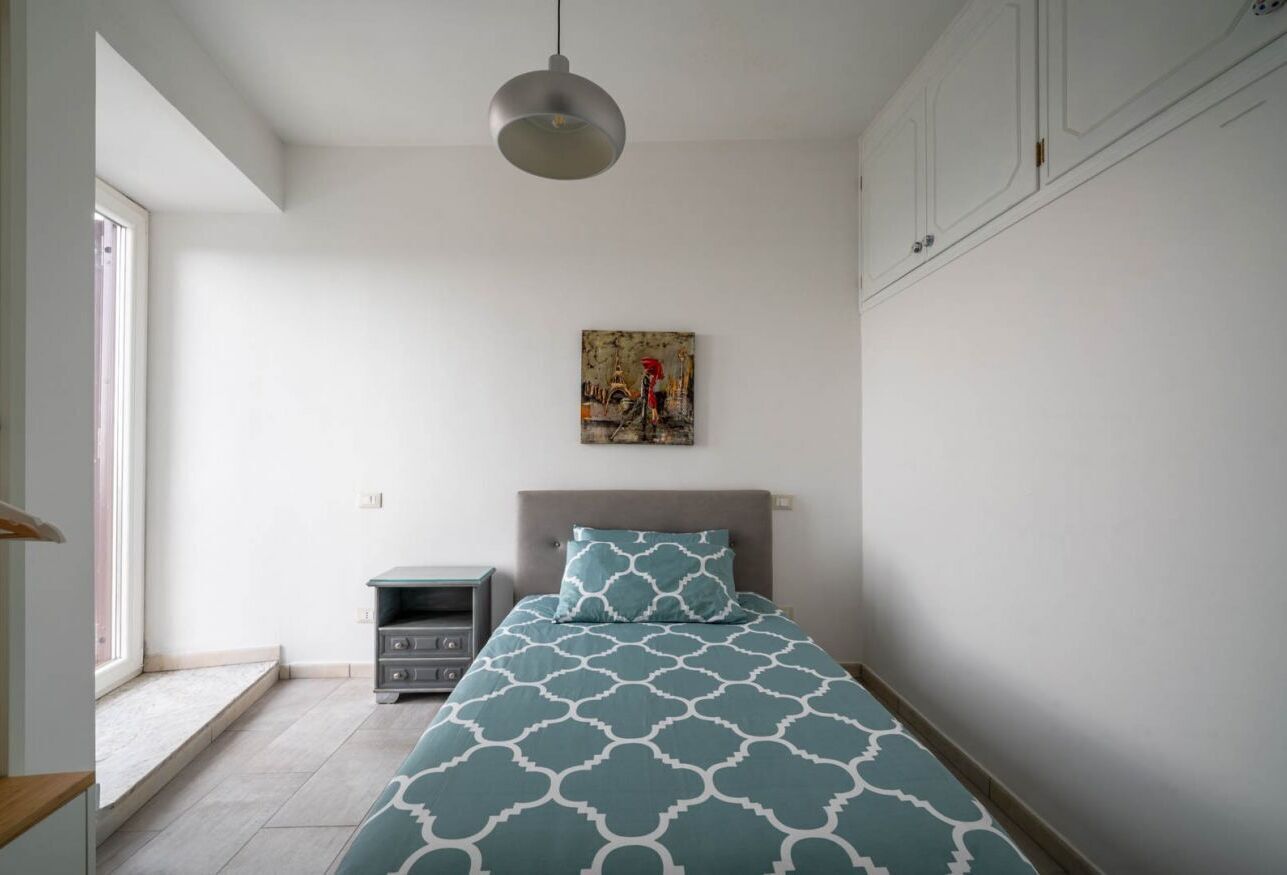 Un dormitorio con cama, mesita de noche, un cuadro y una ventana.