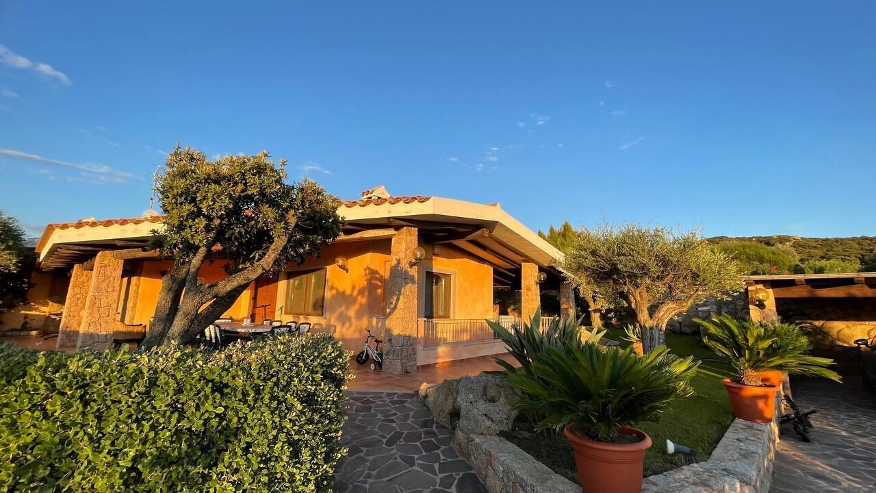 A Mediterranean-style villa with a stone facade, a tiled roof, and a paved patio area with potted plants.