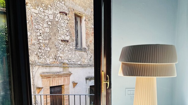 A modern interior with a glass door leading to an outdoor area featuring a stone building and a metal gate. - Casetta della Morica alle Gole Del Nera (Stifone)