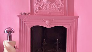 A room with a pink wall, a fireplace with a decorative panel above it, a red sofa, and a white side table with a lamp. - Casetta della Morica alle Gole Del Nera (Stifone)