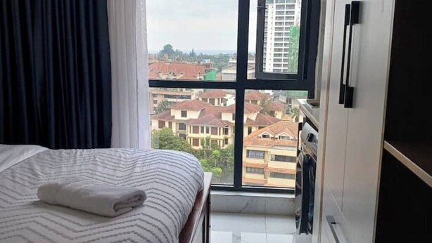 A bedroom with a bed, a window with a city view, and a wardrobe. - Smile's Home (Nairobi)