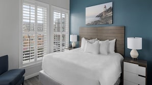 A hotel room with a large bed, two bedside tables with lamps, a chair, and a painting of a lighthouse on the wall.