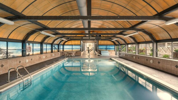An indoor swimming pool with a view of the beach through large windows.