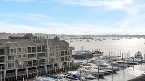 A marina with multiple boats docked, a building with balconies, and a clear sky.
