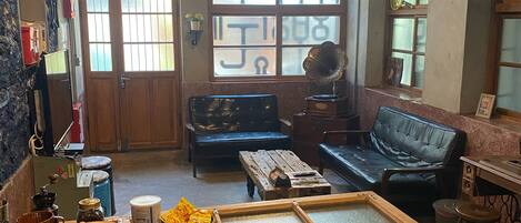 A cozy living area with a wooden coffee table, a black leather sofa, and a dining table with stools. There is a kitchen area with a refrigerator and a sink.