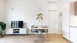 Una sala de estar moderna con una televisión de pantalla plana, una mesa de comedor para cuatro personas y una planta en maceta.
