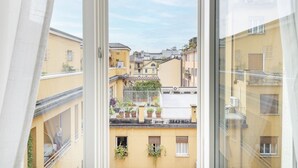 Vista a través de una ventana que muestra un edificio con balcones, plantas en macetas y un cielo despejado.