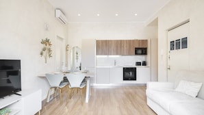 Una sala de estar moderna con un sofá blanco, un comedor con sillas blancas y una cocina con armarios de madera y un microondas.