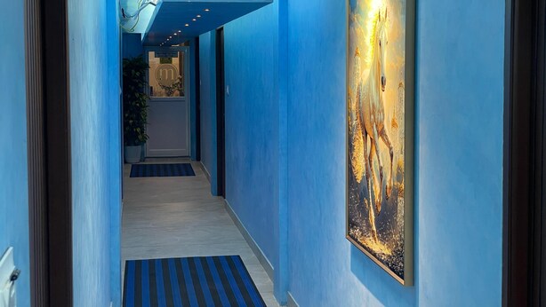 A hallway with blue walls, a large painting on the right, and a door at the end. - Cool hotel with AC in vibrant Kozhikode (Kozhikode)