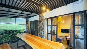 Un interior moderno con una mesa de comedor de madera, paredes de piedra y vistas al verdor exterior.