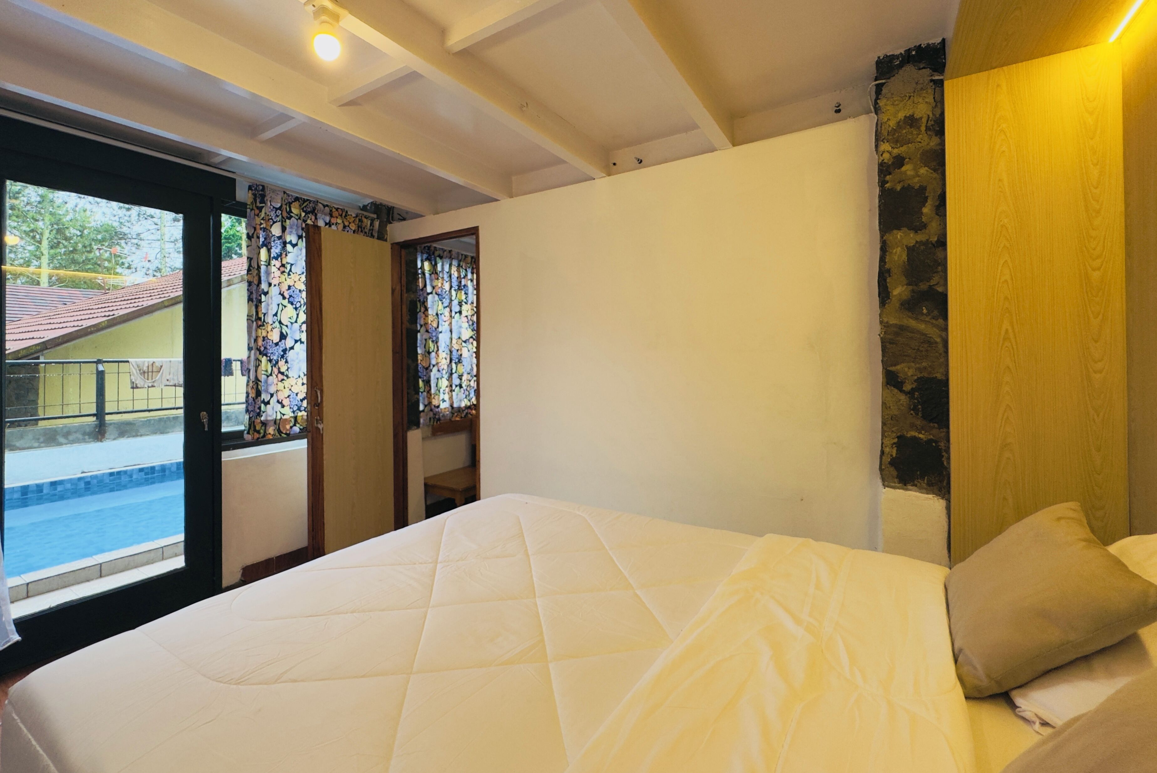 A bedroom with a bed, a window with curtains, and a view of the outside.