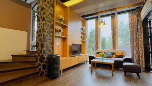 Una sala de estar moderna con un pilar de piedra, muebles de madera, un televisor y ventanas grandes con cortinas.