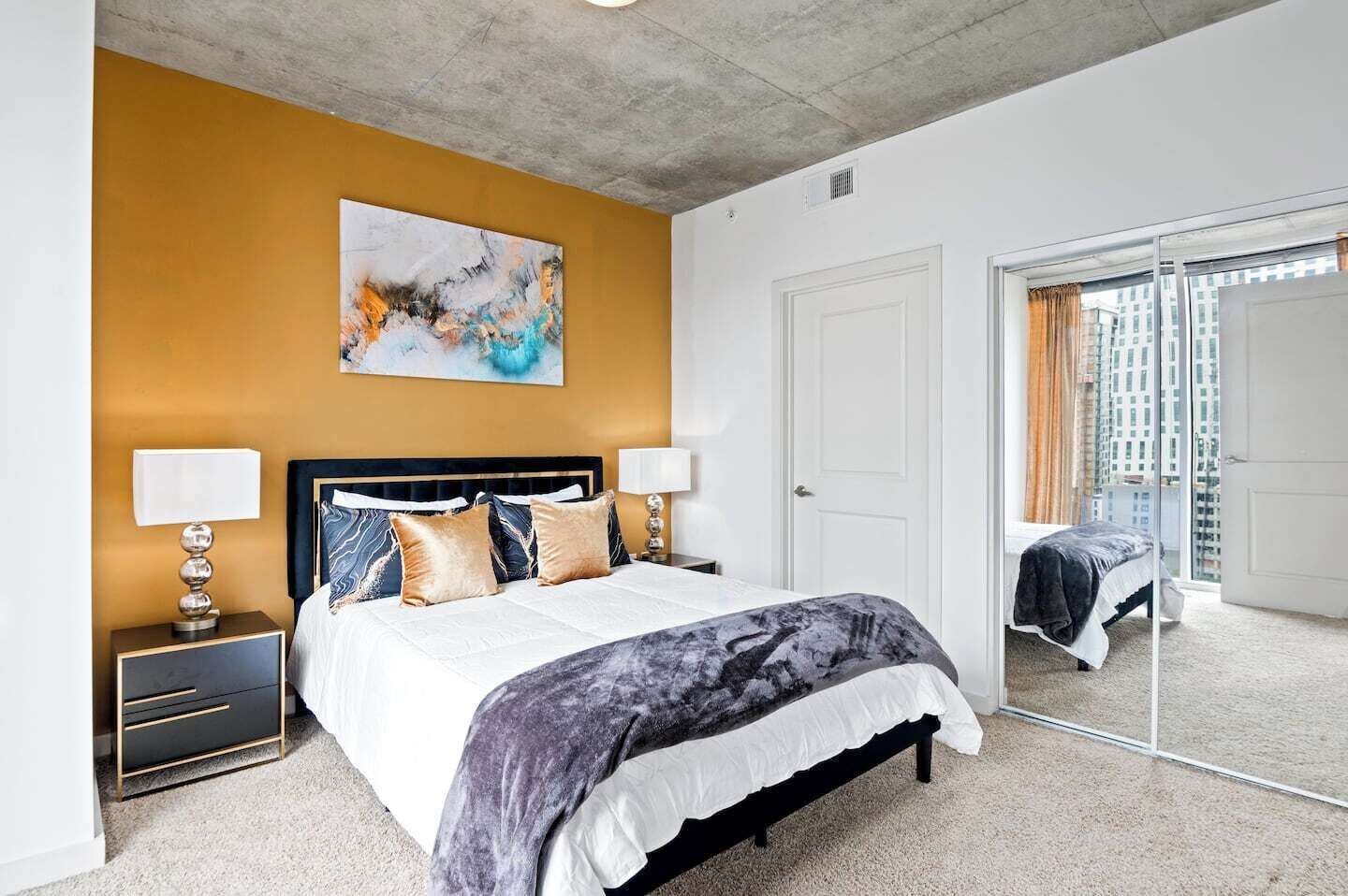 A modern bedroom with a large bed, a nightstand, a wall art piece, and a sliding glass door leading to a balcony.