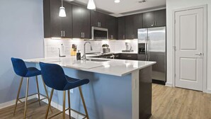 A modern kitchen with dark cabinets, a stainless steel refrigerator, a white countertop island, and two blue bar stools.