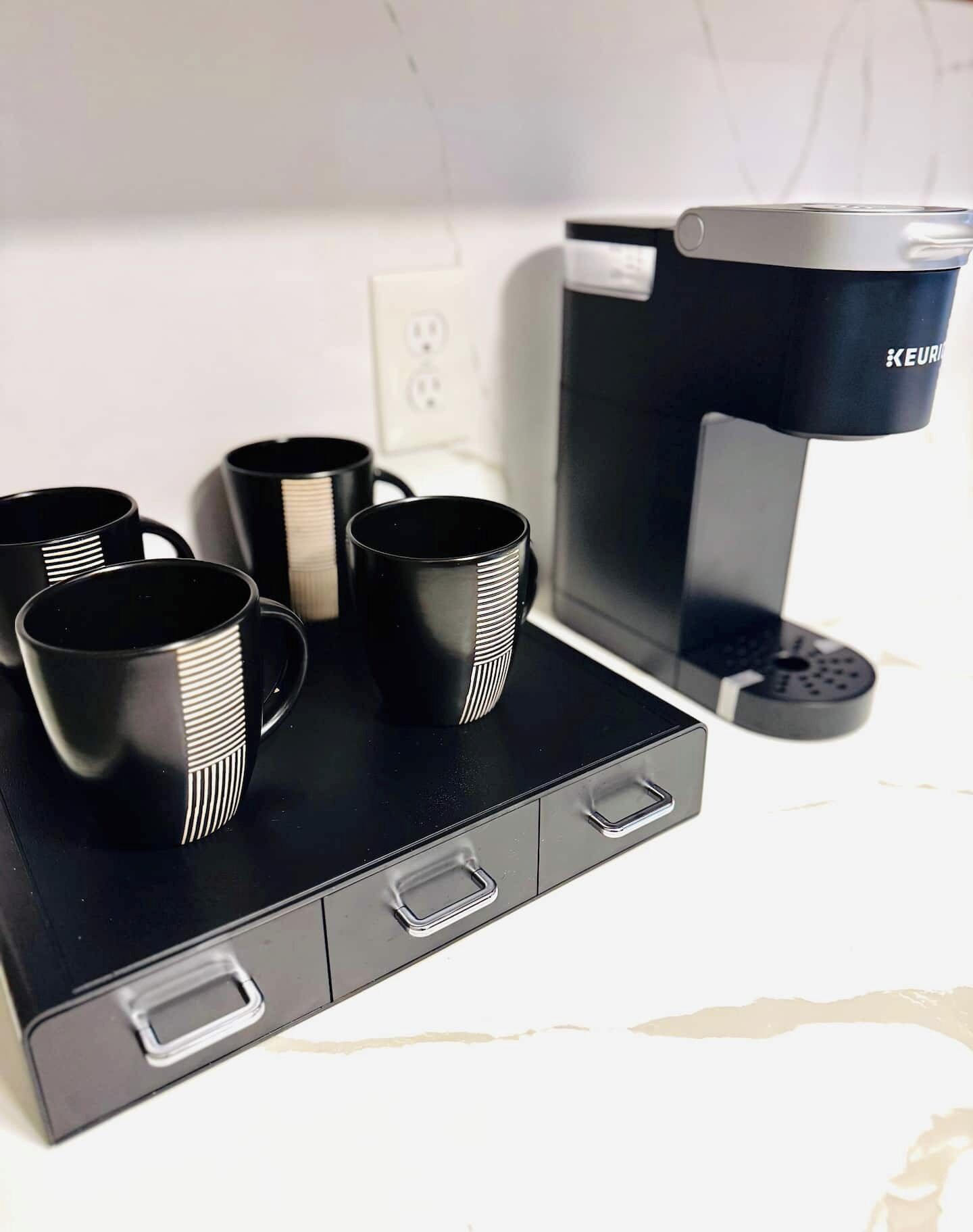 Une machine à café avec quatre tasses noires posées sur un plateau noir.