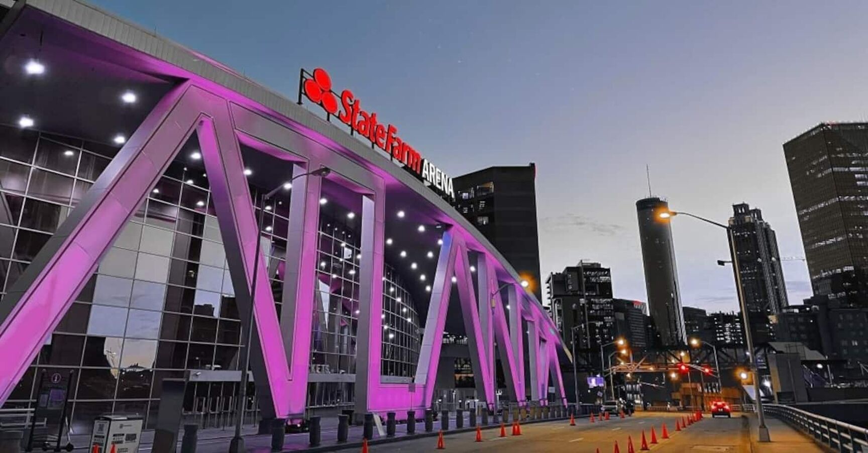 A modern building with a prominent 'State Farm Arena' sign, featuring a unique architectural design with large glass windows and purple lighting accents.