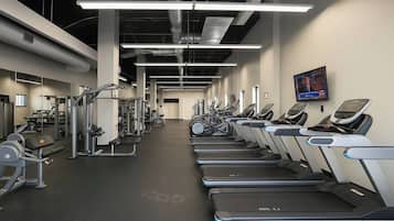 A gym with treadmills, weight machines, and a television screen on the wall.