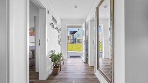 A hallway with a wooden floor, a large mirror, and a potted plant.