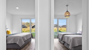 A modern bedroom with two beds, a large window, and a hanging light fixture.