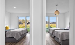 Une chambre moderne avec deux lits, une grande fenêtre et un luminaire suspendu.