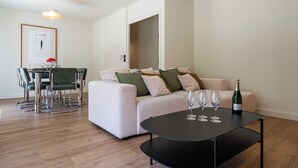 Un salon moderne avec un canapé, une table à manger et des chaises, ainsi qu’une table basse noire sur laquelle se trouvent des verres à vin et une bouteille.